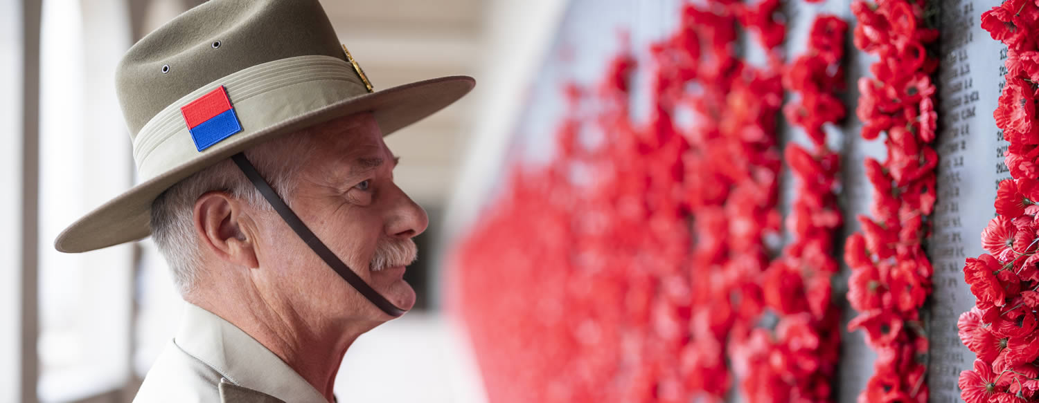 A veteran in the army uniform looking at the wall with poppies.