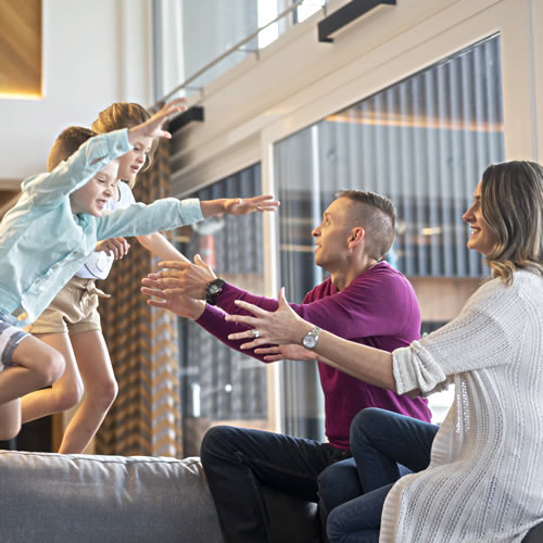Two children leaping off furniture while their parents prepare to catch them.
