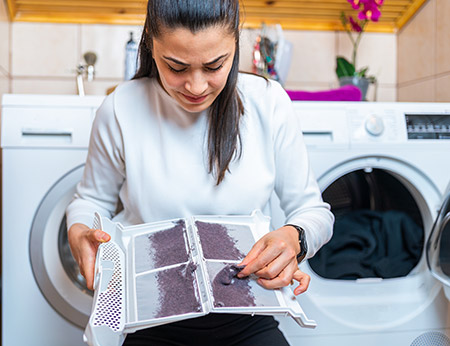 A woman cleaning lint out of a tumble dryer lint filter.