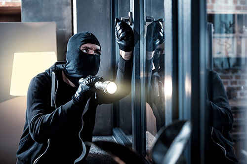 A man with a masked face using torch light breaking into to a house